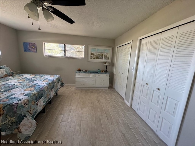 bedroom with a textured ceiling, light wood finished floors, a ceiling fan, and multiple closets