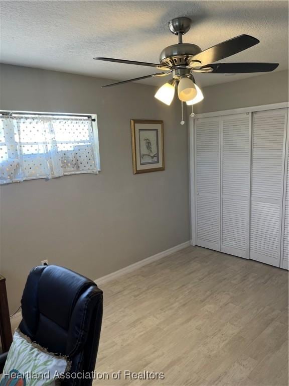 unfurnished bedroom featuring a textured ceiling, light wood finished floors, a ceiling fan, and baseboards