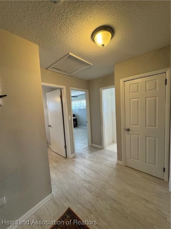 hall featuring light wood-style floors, attic access, baseboards, and a textured ceiling