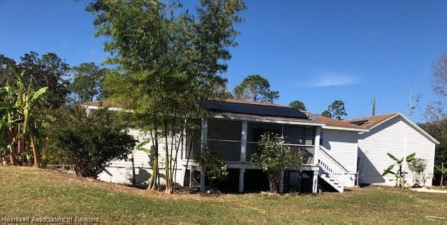 rear view of house featuring solar panels, a sunroom, and a lawn