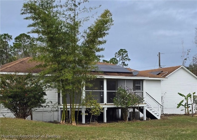 rear view of house with a lawn, a sunroom, and solar panels