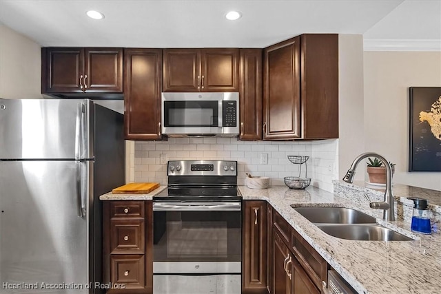 kitchen with light stone countertops, sink, backsplash, appliances with stainless steel finishes, and ornamental molding