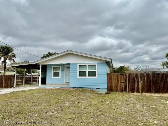 view of front of property featuring concrete driveway, an attached carport, a front lawn, and fence