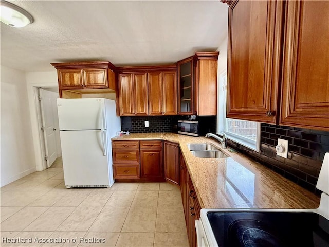 kitchen with light tile patterned floors, glass insert cabinets, freestanding refrigerator, light stone countertops, and a sink