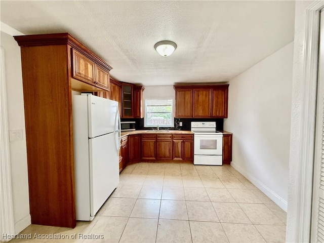 kitchen with light countertops, glass insert cabinets, brown cabinetry, a textured ceiling, and white appliances