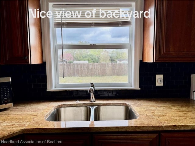 kitchen with light stone counters, stainless steel microwave, decorative backsplash, and a sink