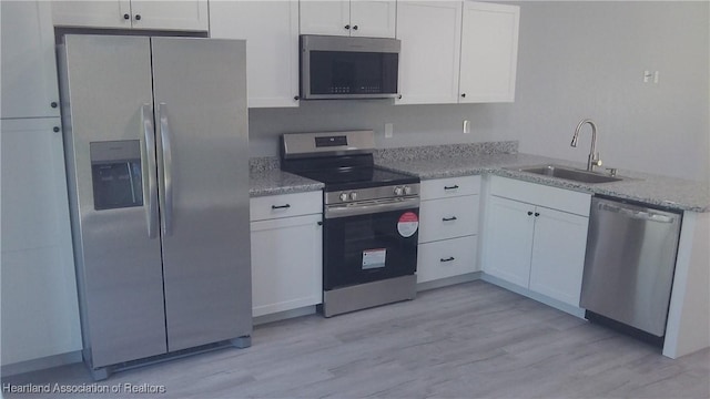 kitchen with white cabinetry, appliances with stainless steel finishes, light stone countertops, and sink