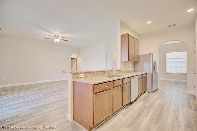 kitchen with light stone countertops, appliances with stainless steel finishes, sink, light hardwood / wood-style flooring, and ceiling fan