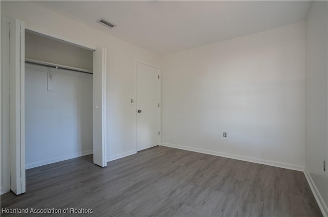 unfurnished bedroom with baseboards, visible vents, wood finished floors, and a closet