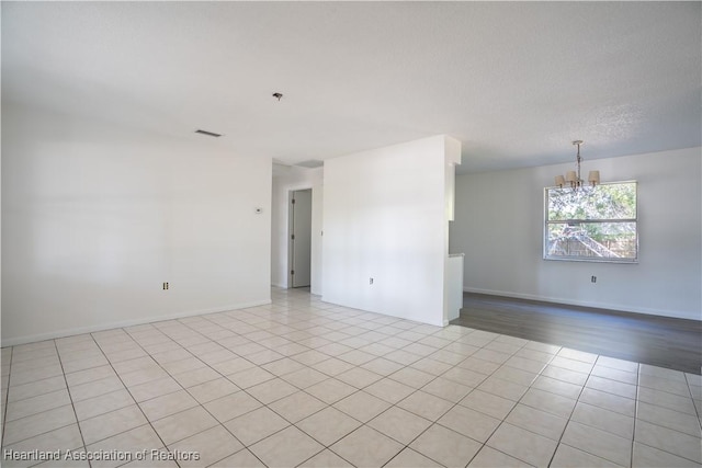 empty room with visible vents, light tile patterned flooring, and a chandelier