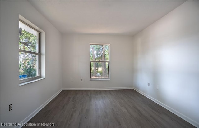 spare room with dark wood-type flooring, baseboards, and a healthy amount of sunlight
