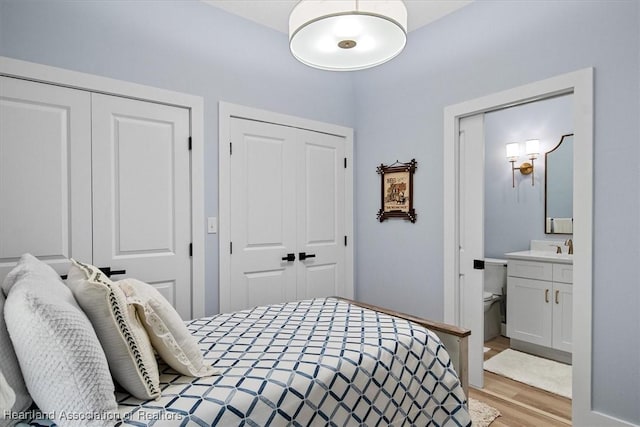 bedroom featuring light wood-type flooring, two closets, and ensuite bath