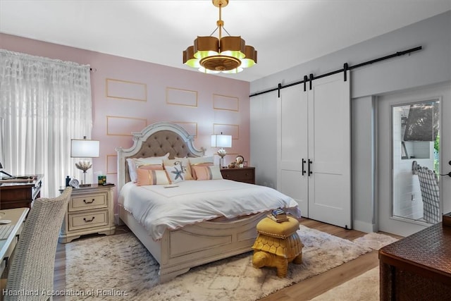 bedroom with a barn door, light hardwood / wood-style floors, and a notable chandelier