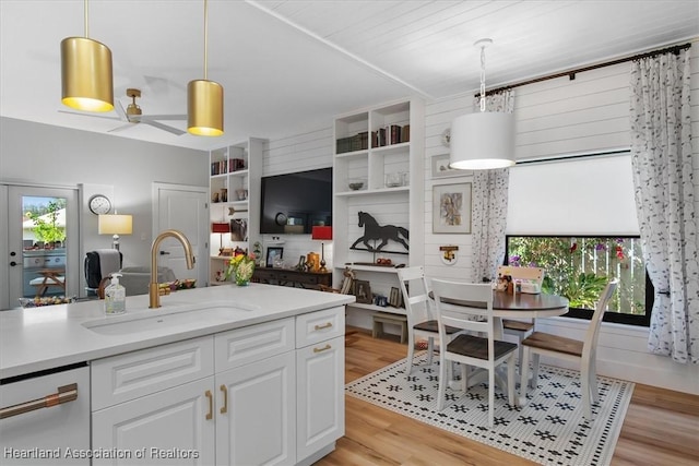 kitchen with pendant lighting, dishwasher, sink, light wood-type flooring, and white cabinetry