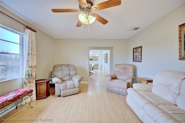 living room featuring ceiling fan, light hardwood / wood-style floors, and a textured ceiling