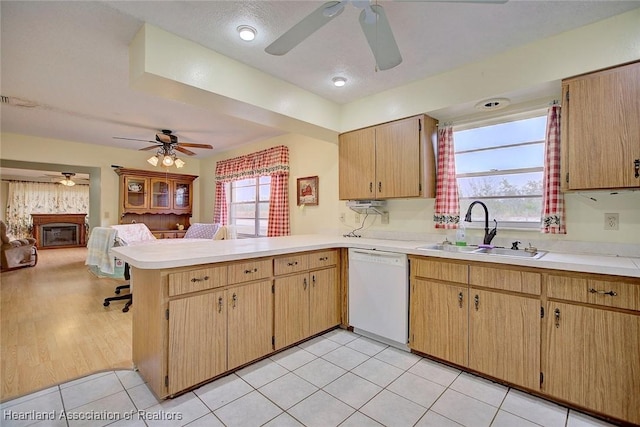 kitchen featuring dishwasher, sink, light tile patterned floors, kitchen peninsula, and a healthy amount of sunlight