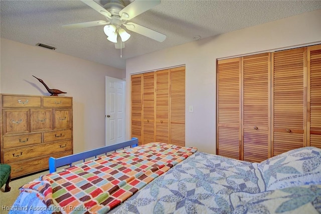 bedroom featuring multiple closets, ceiling fan, carpet, and a textured ceiling