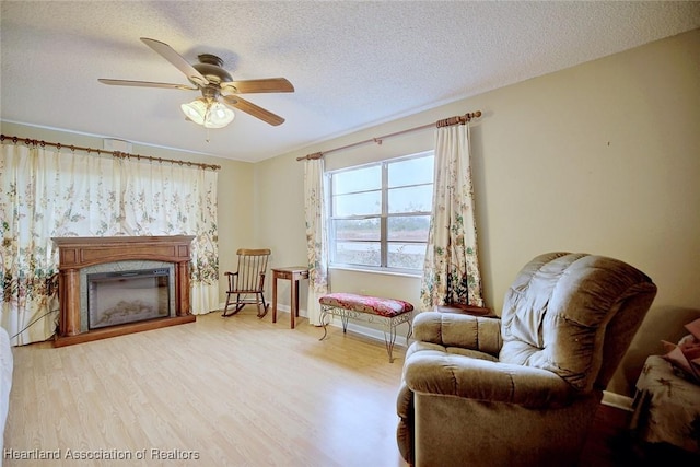 living area with ceiling fan, a textured ceiling, and light hardwood / wood-style flooring