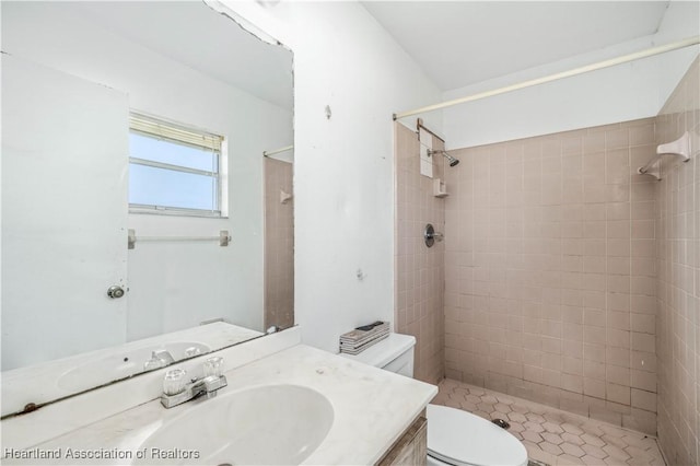 bathroom with a tile shower, vanity, and toilet