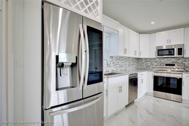 kitchen featuring tasteful backsplash, light stone counters, stainless steel appliances, sink, and white cabinetry