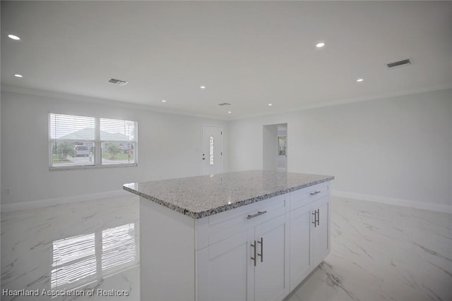 kitchen featuring a center island, white cabinetry, crown molding, and light stone counters