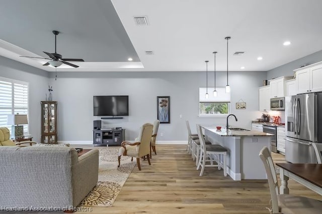 living room with sink, light hardwood / wood-style floors, a raised ceiling, and ceiling fan