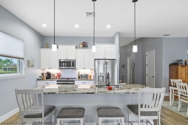 kitchen with pendant lighting, appliances with stainless steel finishes, tasteful backsplash, an island with sink, and white cabinets