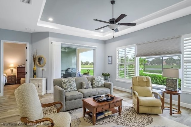 living room featuring ceiling fan, a raised ceiling, and light hardwood / wood-style floors