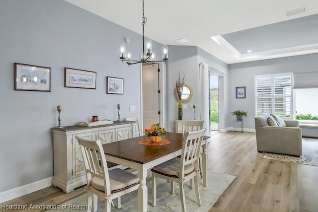 dining room with a raised ceiling, an inviting chandelier, and light hardwood / wood-style flooring