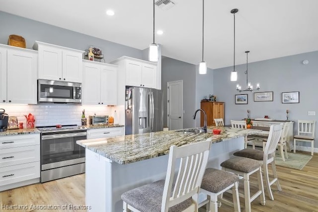 kitchen with hanging light fixtures, white cabinetry, appliances with stainless steel finishes, and a kitchen island with sink