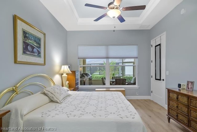 bedroom with ceiling fan, a raised ceiling, and light hardwood / wood-style flooring