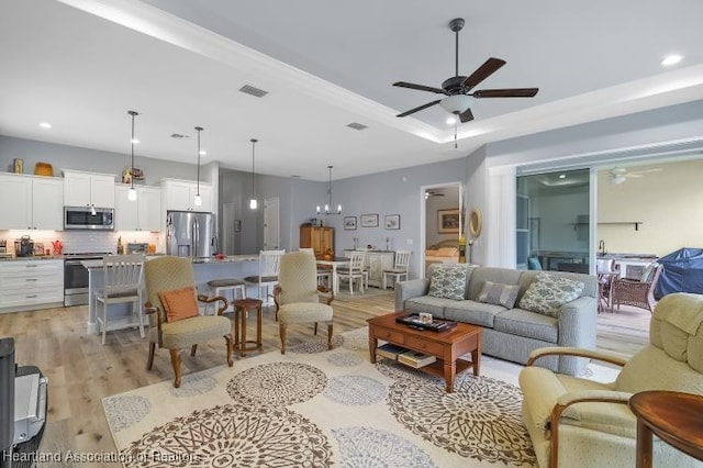 living room with a tray ceiling, ceiling fan with notable chandelier, and light hardwood / wood-style floors