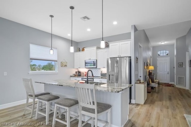 kitchen with white cabinetry, appliances with stainless steel finishes, a kitchen island with sink, and pendant lighting