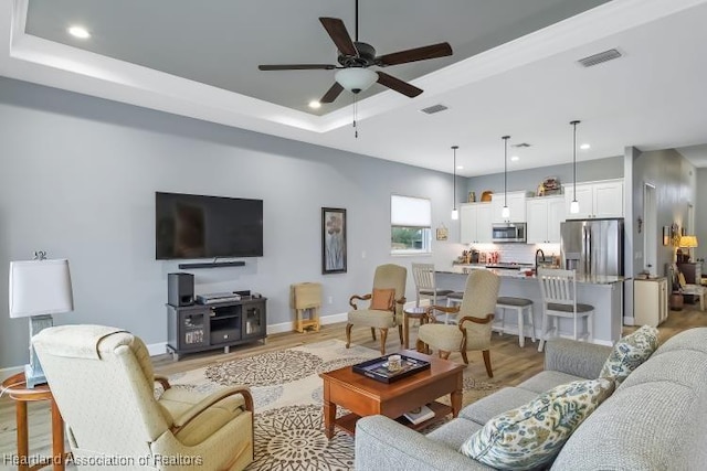 living room featuring ceiling fan, a tray ceiling, and light wood-type flooring