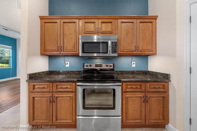kitchen with appliances with stainless steel finishes, dark stone countertops, and brown cabinets