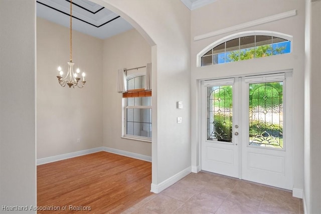 foyer with light wood-style flooring, a chandelier, baseboards, arched walkways, and french doors