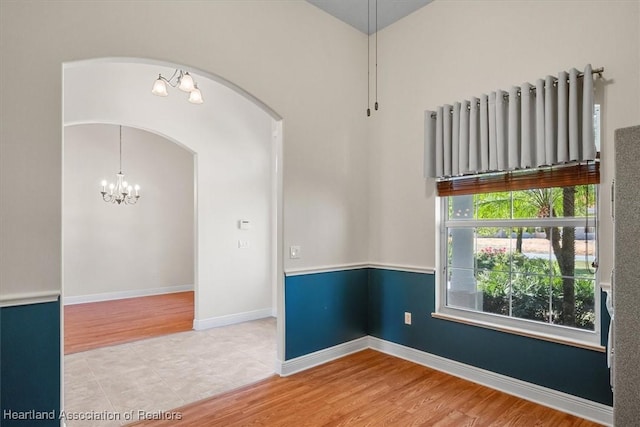 unfurnished room featuring arched walkways, baseboards, wood finished floors, and a chandelier