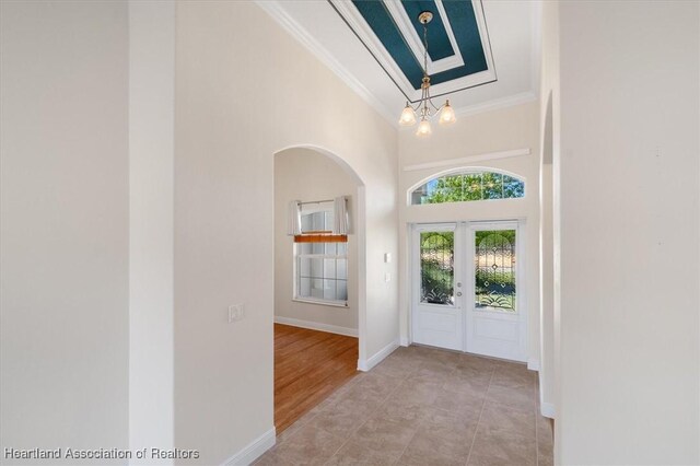 foyer entrance featuring high vaulted ceiling, baseboards, ornamental molding, arched walkways, and a notable chandelier