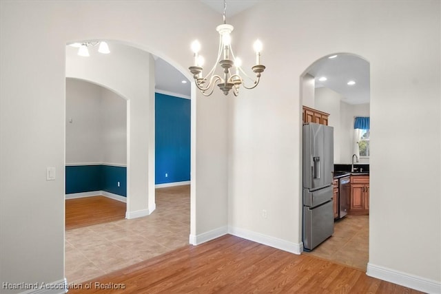 interior space with arched walkways, baseboards, an inviting chandelier, and light wood-type flooring
