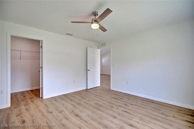 unfurnished bedroom with a closet, a walk in closet, light hardwood / wood-style floors, and ceiling fan