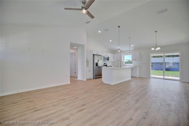 kitchen featuring a kitchen island with sink, high vaulted ceiling, appliances with stainless steel finishes, decorative light fixtures, and white cabinetry