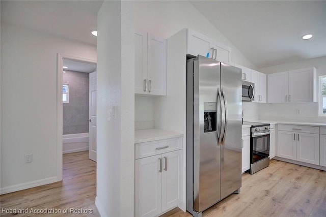 kitchen with light wood-type flooring, white cabinetry, appliances with stainless steel finishes, and vaulted ceiling