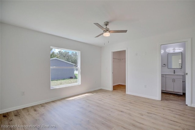 unfurnished bedroom featuring ceiling fan, a spacious closet, connected bathroom, light hardwood / wood-style floors, and a closet