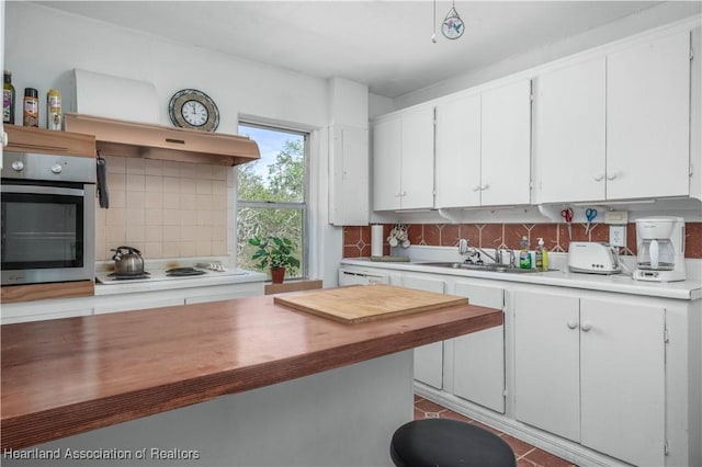 kitchen with white stovetop, sink, white cabinets, decorative backsplash, and stainless steel oven