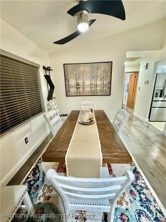 dining room with ceiling fan, wood-type flooring, and vaulted ceiling