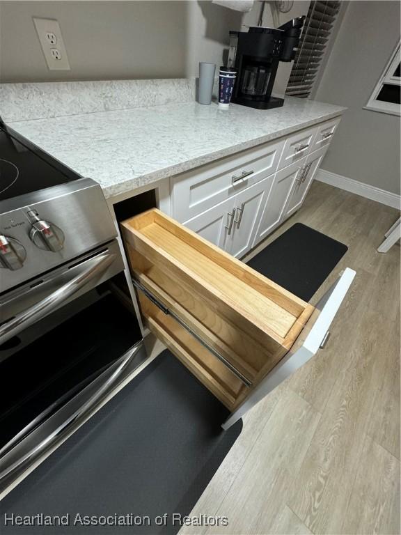 kitchen with white cabinets, light hardwood / wood-style floors, and stainless steel range