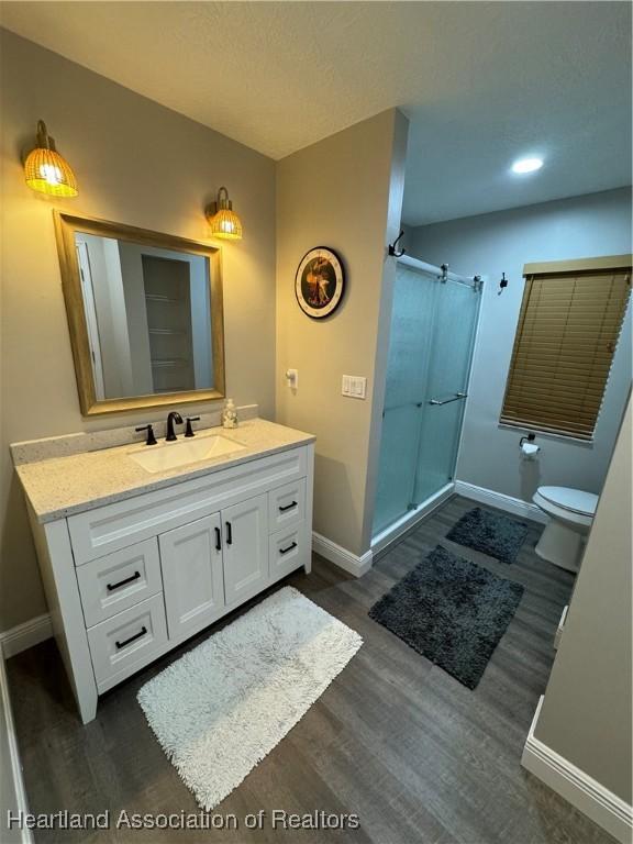 bathroom featuring vanity, wood-type flooring, an enclosed shower, and toilet