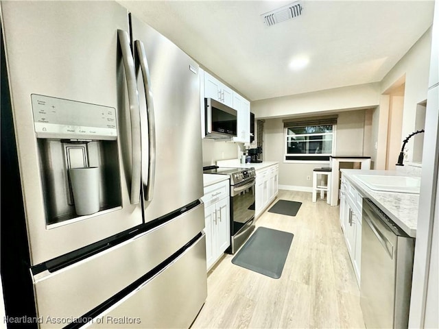 kitchen with white cabinetry, sink, light stone counters, appliances with stainless steel finishes, and light wood-type flooring