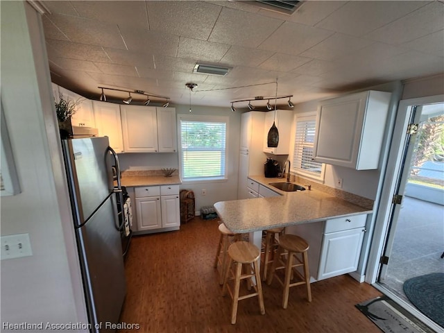 kitchen with kitchen peninsula, a kitchen breakfast bar, pendant lighting, white cabinets, and stainless steel refrigerator