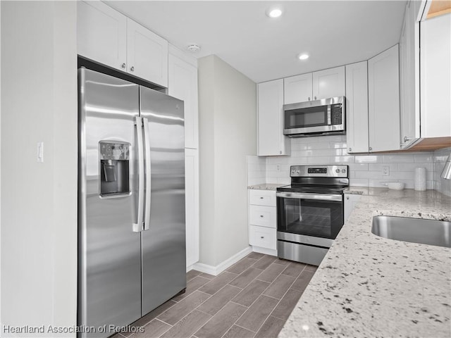 kitchen featuring tasteful backsplash, appliances with stainless steel finishes, white cabinets, and light stone counters